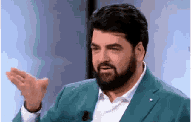 a man with a beard is wearing a green suit and white shirt and making a funny face .