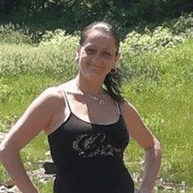 a woman in a black tank top is standing in a grassy field .