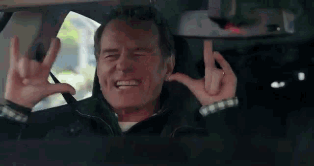 a man is sitting in a car making a devil horns sign with his fingers .