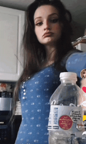 a woman in a blue top holds a bottle of aquafina water in her hand