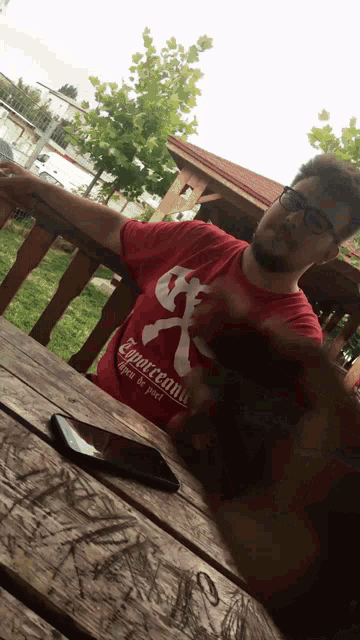 a man wearing a red shirt that says capricornu sits at a picnic table