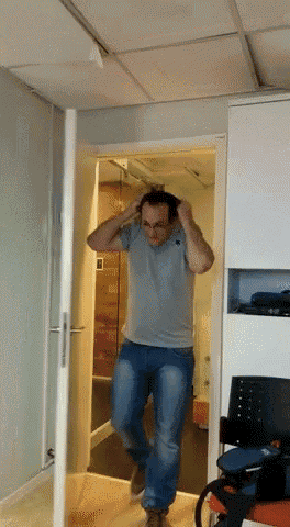 a man in a grey shirt and blue jeans is walking through a doorway