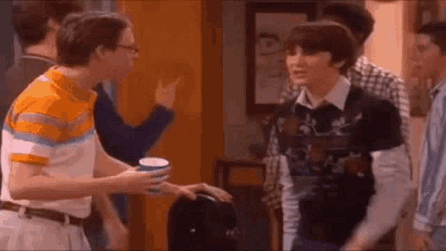 a group of young men are standing next to each other in a room and talking to each other .