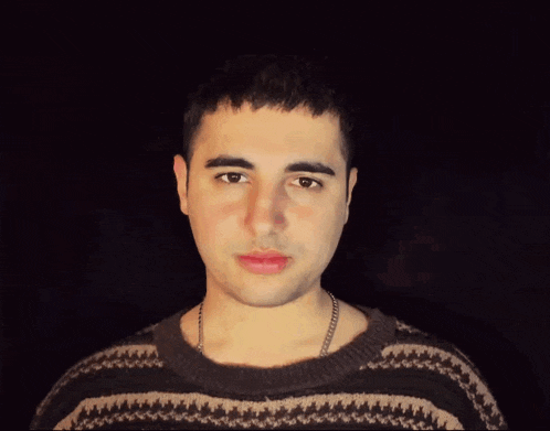 a man wearing a sweater and a chain around his neck looks at the camera