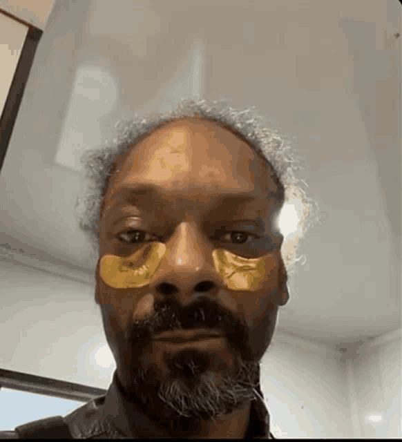 a man with a beard and gold eye patches on his face .