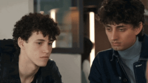 two young men with curly hair are looking at each other in a blurry photo taken by a person named joay jones