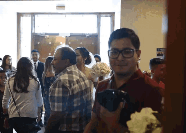 a man holding a camera stands in front of a group of people at a wedding