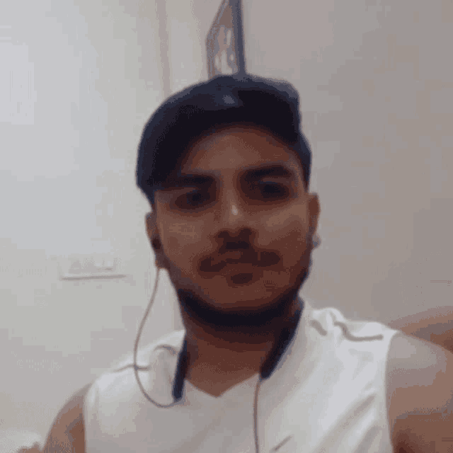 a man with a beard wearing a white tank top and headphones