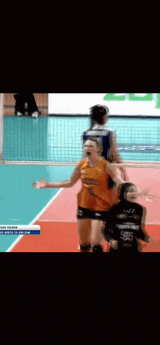 a woman in an orange shirt is standing on a volleyball court with her arms in the air