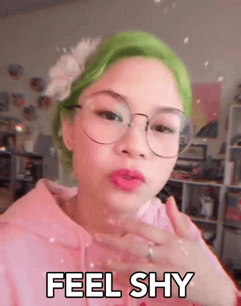 a girl with green hair is wearing glasses and a pink hoodie and says feel shy