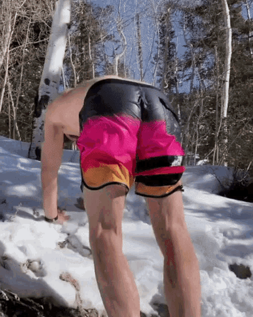a man in a pair of pink and orange shorts is bending over in the snow