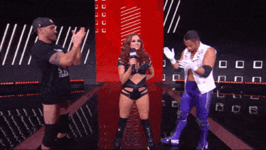 a female wrestler is talking into a microphone while two men applaud her