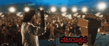 a man is singing into a microphone in front of a crowd with a sign that says ' natraman '