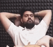 a man with a beard is sitting in a chair with his hands behind his head and his eyes closed .