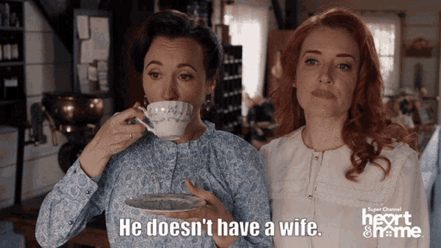 two women standing next to each other with one saying he does n't have a wife while drinking from a cup