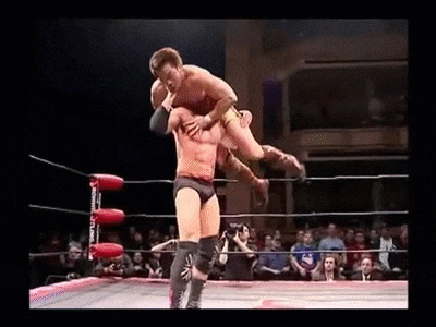 two men are wrestling in a wrestling ring and one of them is carrying the other on his back .