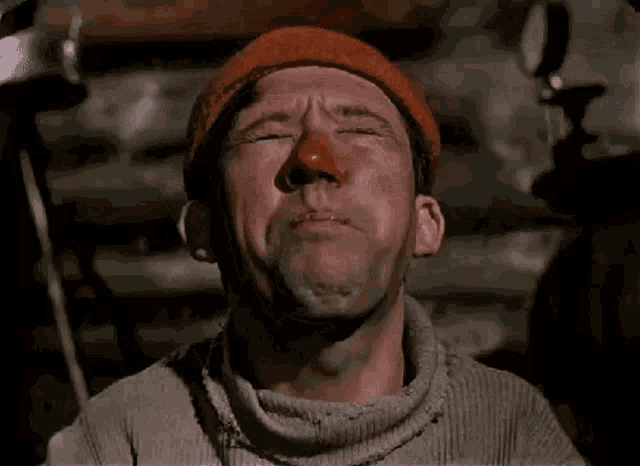 a man with a red nose and a beanie is crying with his eyes closed .