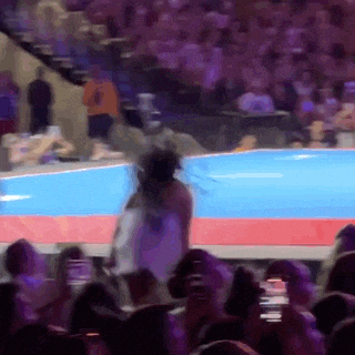 a woman in a white dress is walking on a stage in front of a crowd of people .