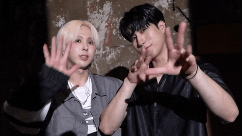 two young men are standing next to each other and making a heart with their hands .