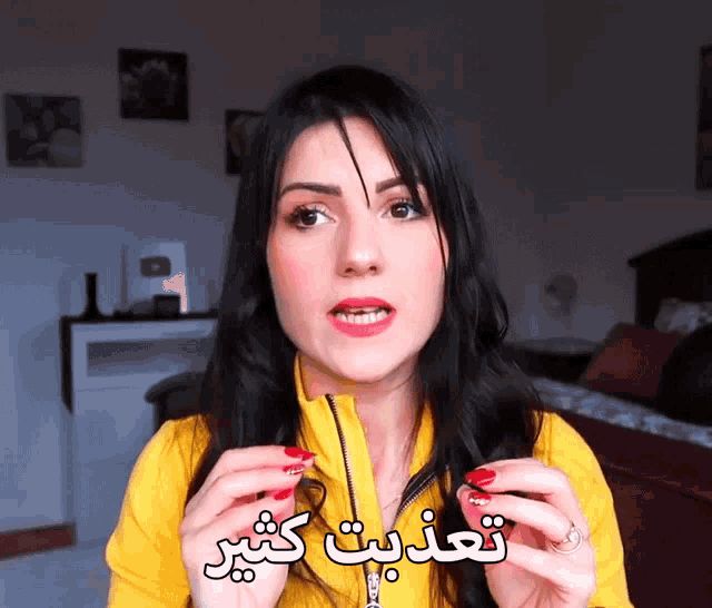 a woman in a yellow jacket holds something in her hands with arabic writing
