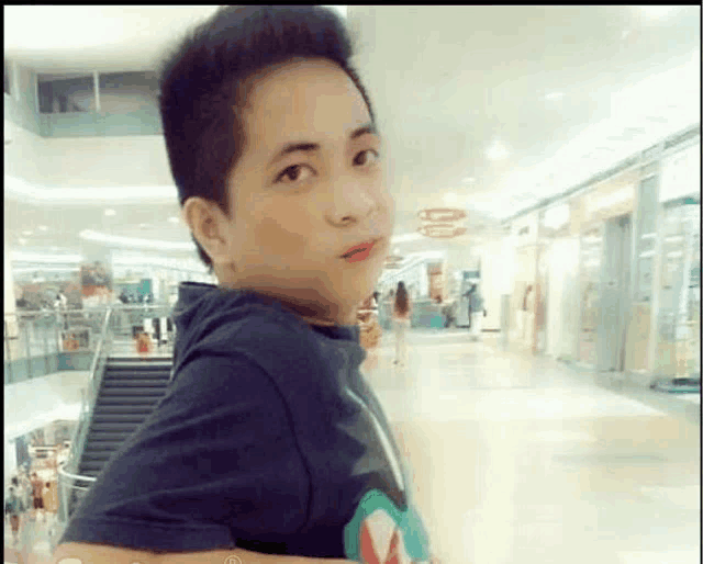 a young boy in a black shirt is standing in a mall looking at the camera