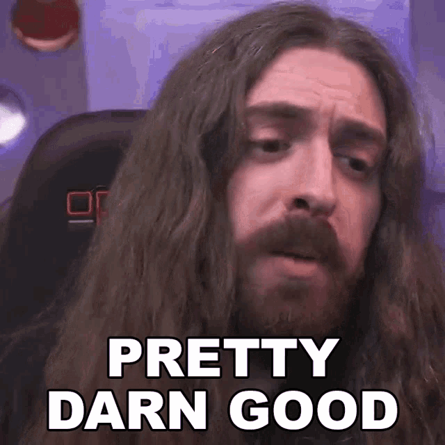 a man with long hair and a beard is sitting in a chair and says pretty darn good .