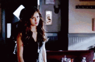 a woman in a black dress is standing in a dark room looking at something .