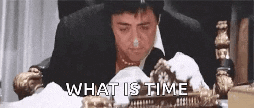 a man in a suit is sitting at a table with a clock in front of him .