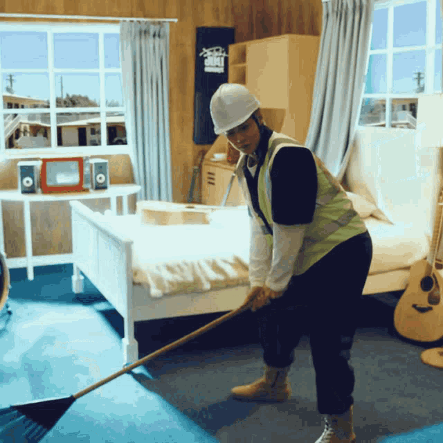 a man wearing a hard hat and safety vest is sweeping a floor in a bedroom