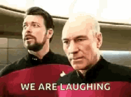 two men are standing next to each other laughing .