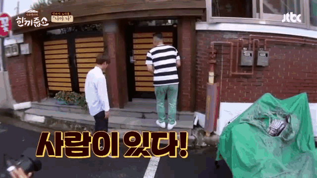 a man in a striped shirt is standing in front of a brick building with a sign that says jtbc