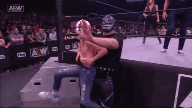 a man in a mask is holding another man in a wrestling ring while a woman watches .