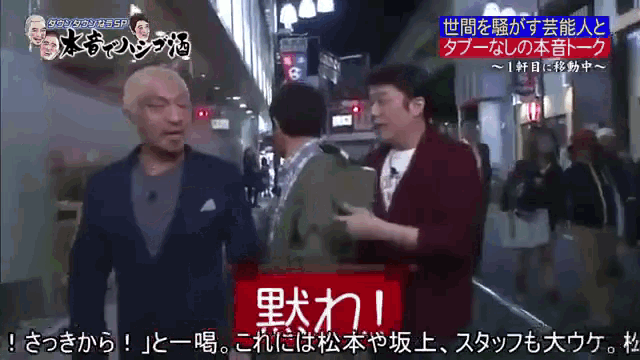 a man in a suit talks to another man in a crowded street with chinese writing on the screen