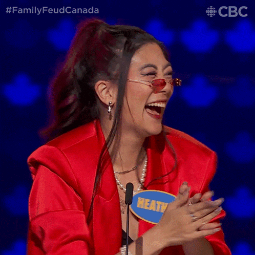 a woman wearing sunglasses and a red jacket is laughing with a name tag that says heatv on it