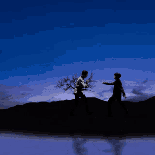 a silhouette of two men standing next to a tree