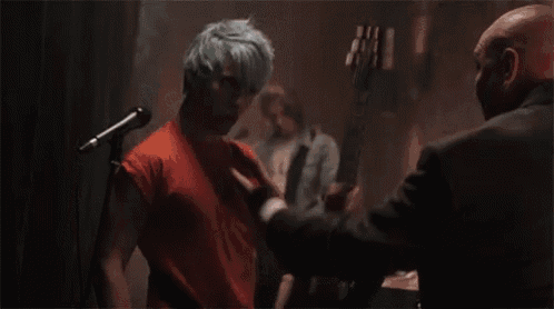 a man with green hair is shaking hands with another man while playing a guitar .