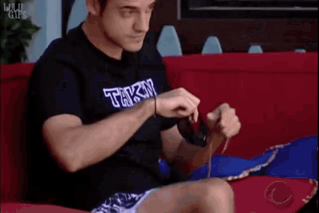 a man is sitting on a couch wearing a black shirt that says tak3n
