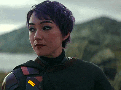 a woman with purple hair is standing in front of a body of water and looking at the camera .