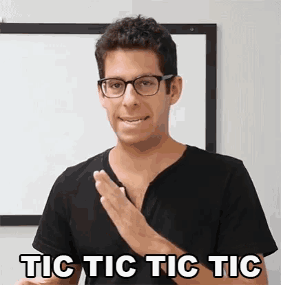a man wearing glasses and a black shirt is giving a tic tac tic tic gesture .