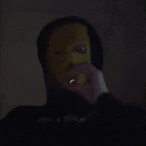 a person wearing a yellow mask and a black hoodie is holding something in their hand .