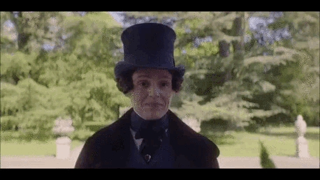 a man in a top hat is standing in a park with trees in the background .
