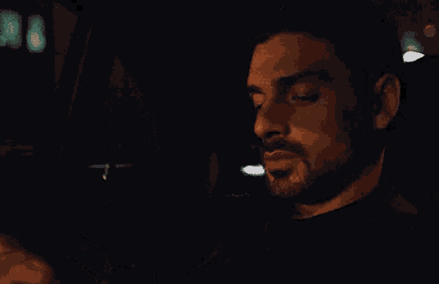 a man with a beard is sitting in the driver 's seat of a car at night .