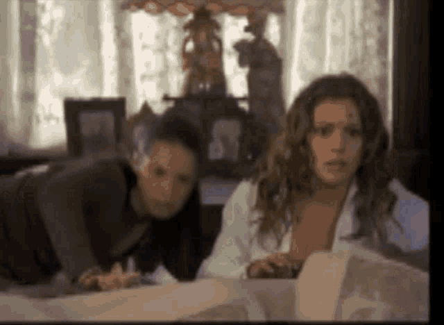 two women are looking at something in a room with a lamp in the background .