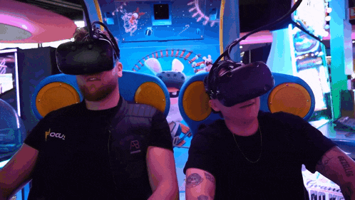 a man wearing a vest that says focus sits next to another man wearing virtual reality glasses