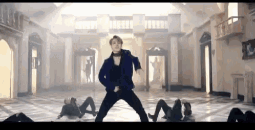a man in a blue jacket is dancing in a large room with other dancers .