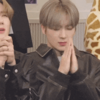 a young man in a leather jacket is praying with his hands folded .