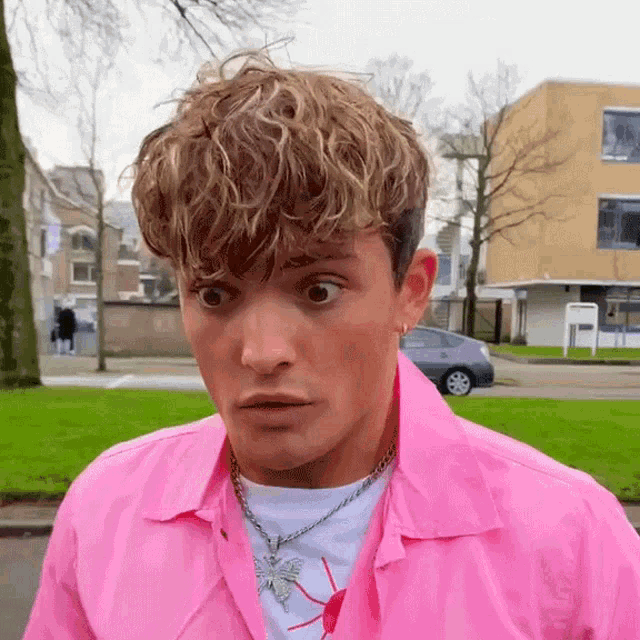 a man wearing a pink shirt and a butterfly necklace is making a funny face