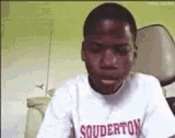 a young boy wearing a souderton shirt is making a face .