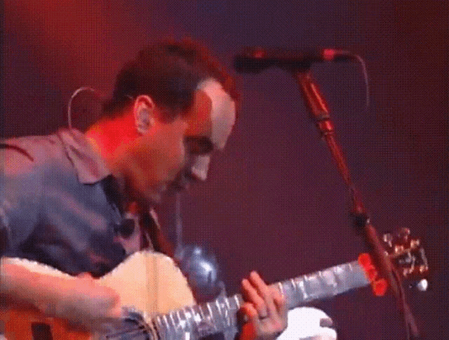a man is playing a guitar in a dark room with a red light behind him
