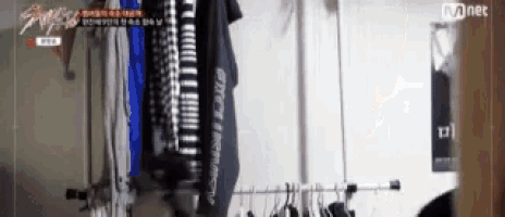 a person is standing in a closet with clothes hanging on a rack .